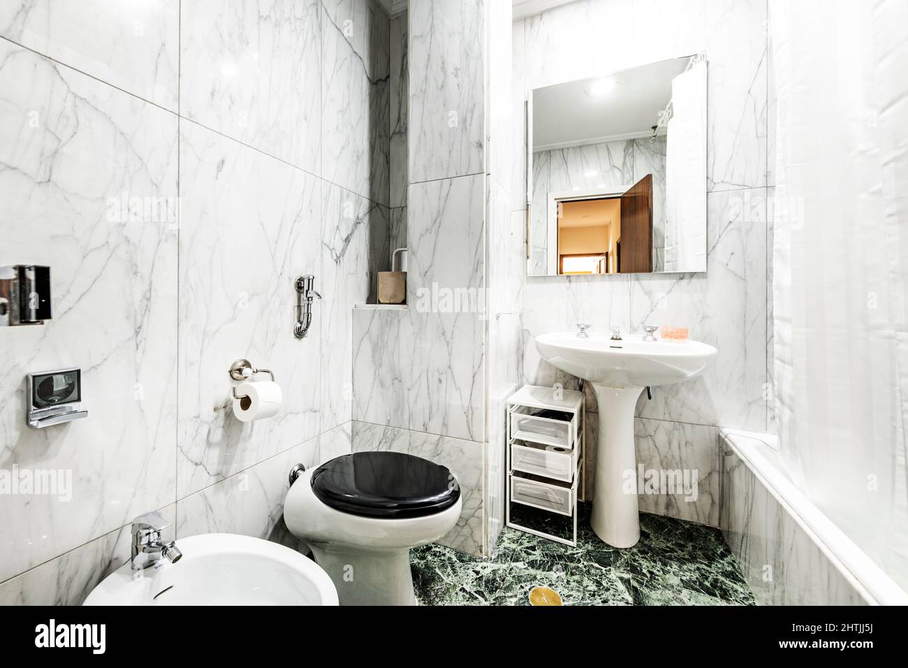 Bathroom clad in large white marble tiles with gray veining on the walls and green marble on the