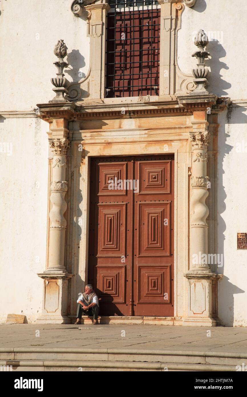 Mann sitzt vor dem Portal der Igreja do Carmo, Karmeliterkirche, Faro, Algarve, Portugal Stock Photo