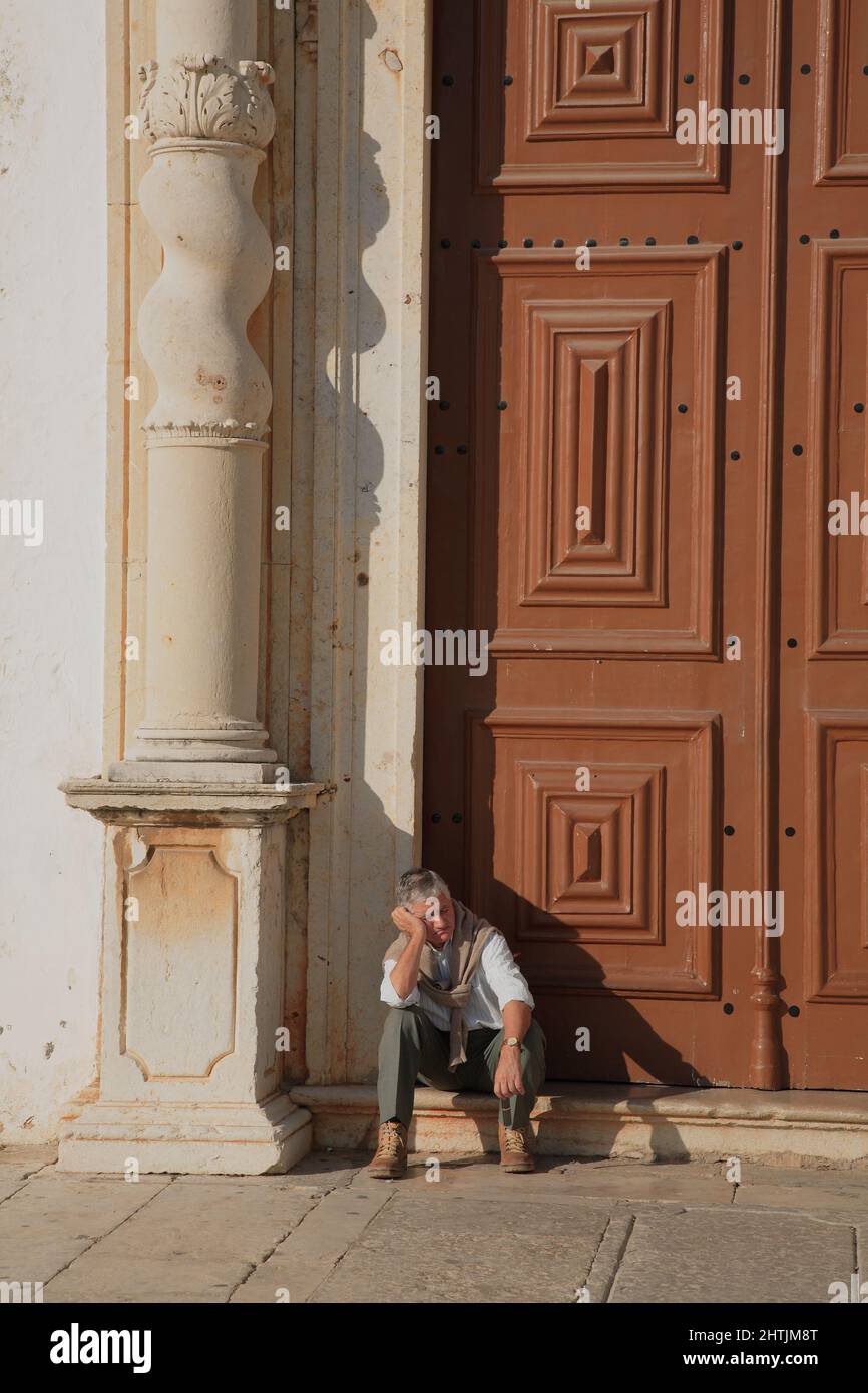 Mann sitzt vor dem Portal der Igreja do Carmo, Karmeliterkirche, Faro, Algarve, Portugal Stock Photo