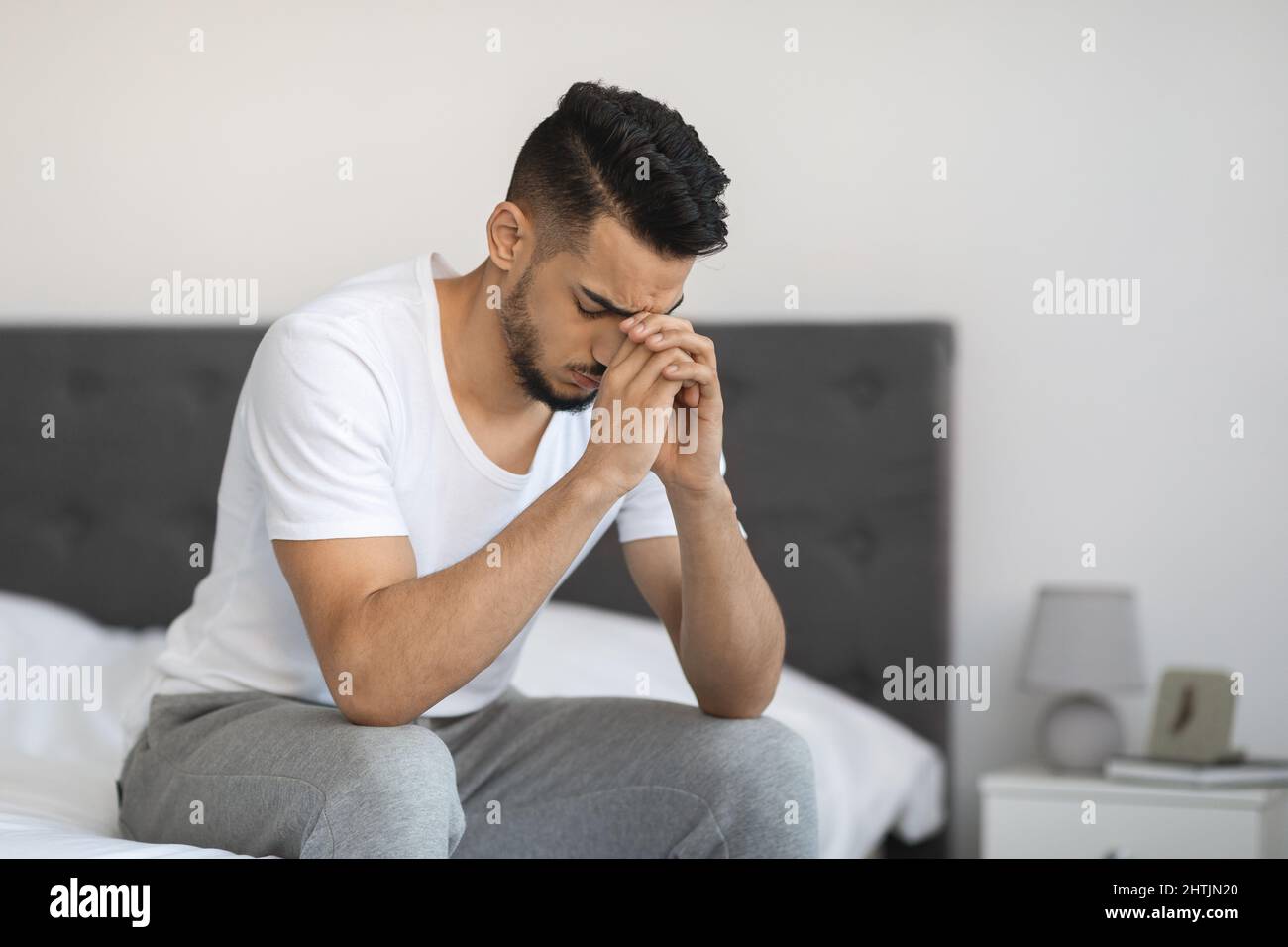 Unhappy and negative young man sits on bed and looks on camera. He