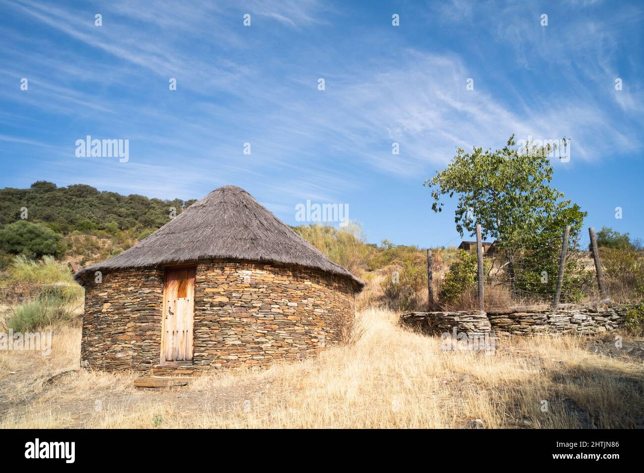 Old cabin or hut with a round shape and slate stone walls and a broom and straw roof Stock Photo