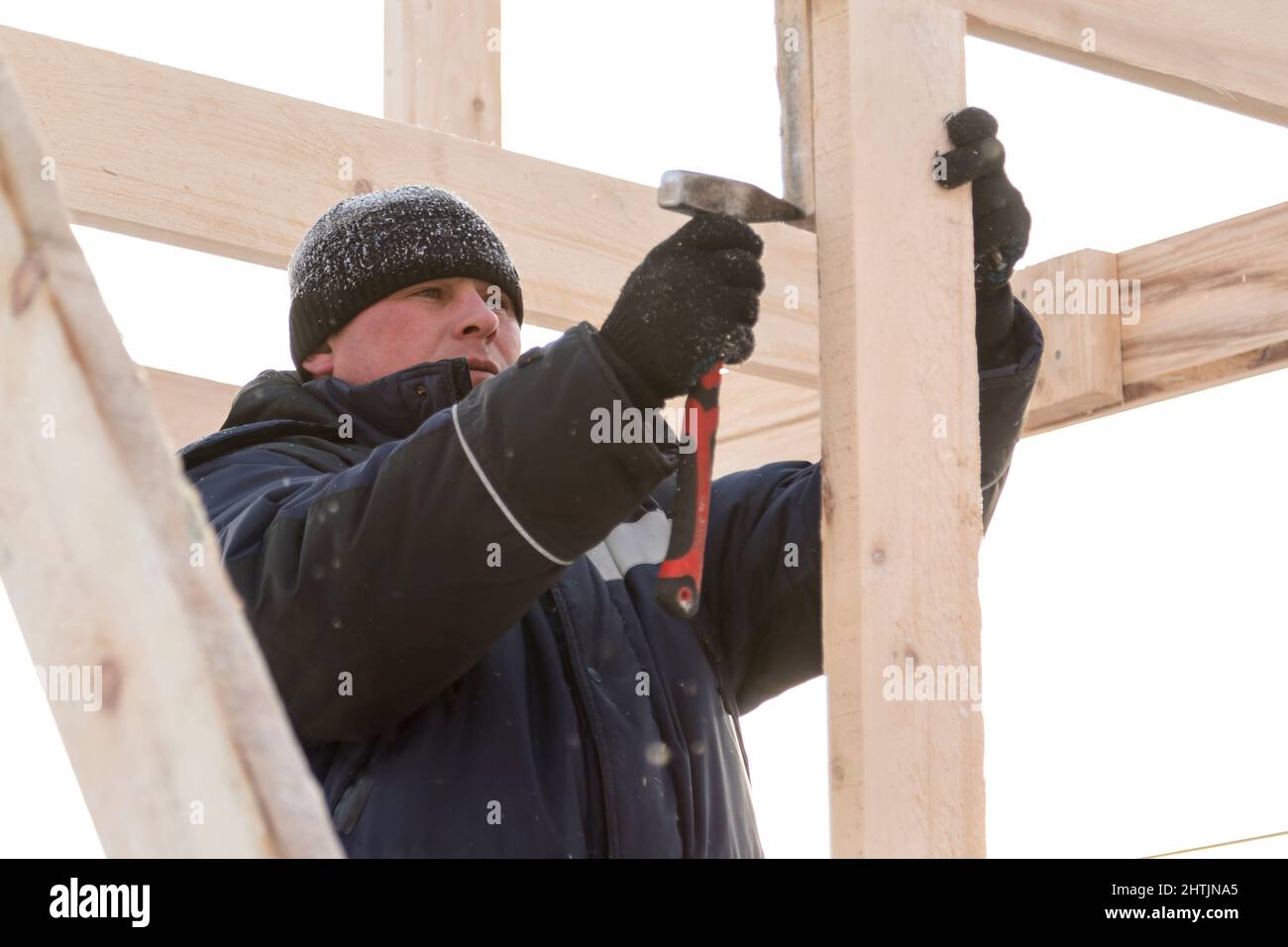 A builder in a blue jacket with a hammer in his hand hammers a nail Stock Photo