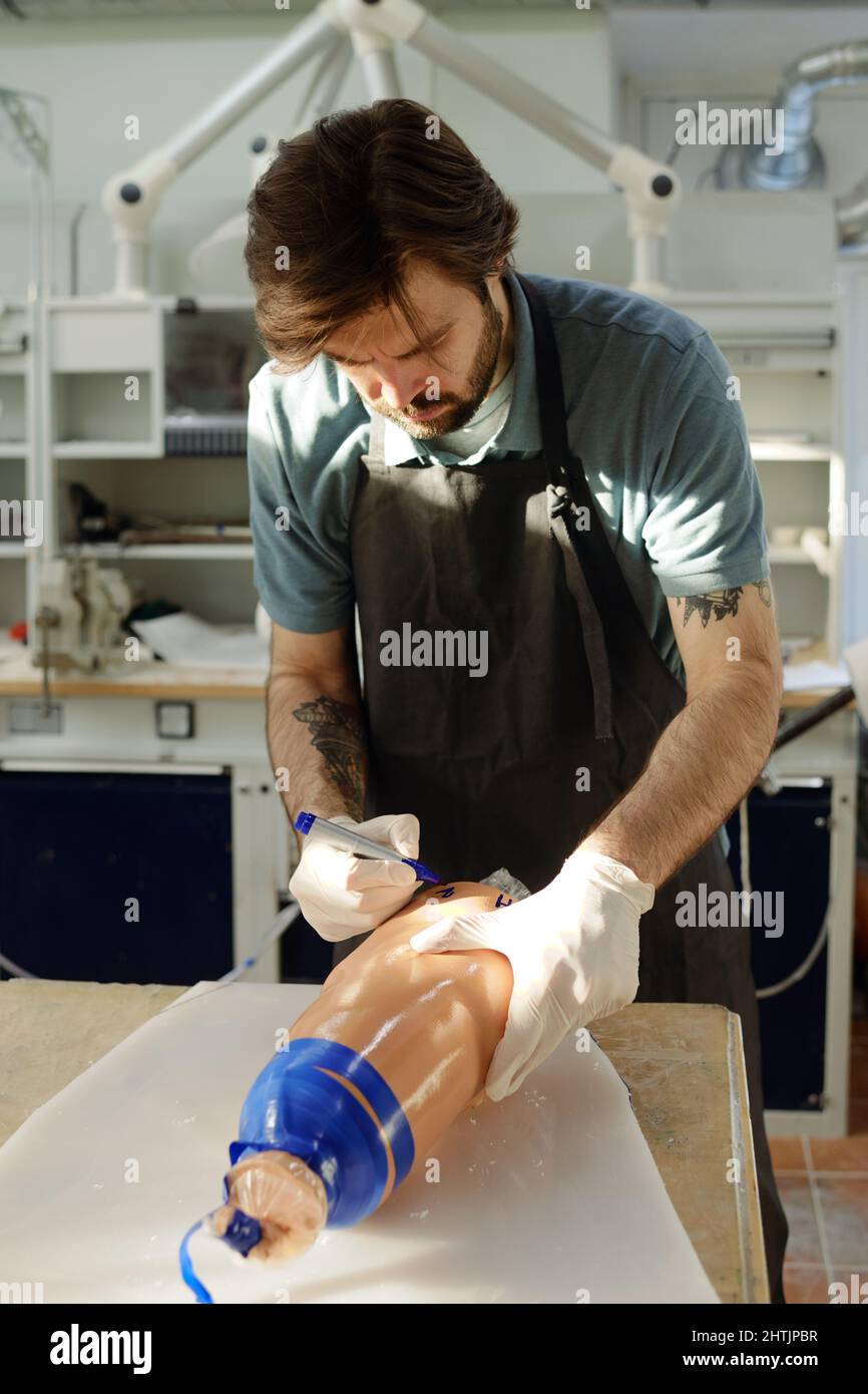 Male worker of prosthetic factory in gloves and apron writing on ...
