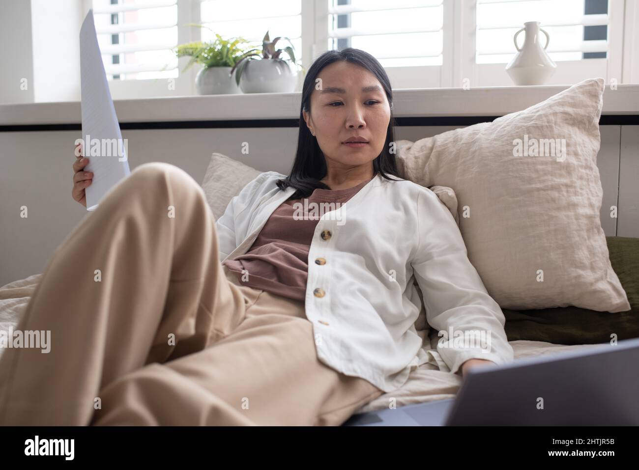 Serious female of Asian ethnicity looking at data on laptop screen ...