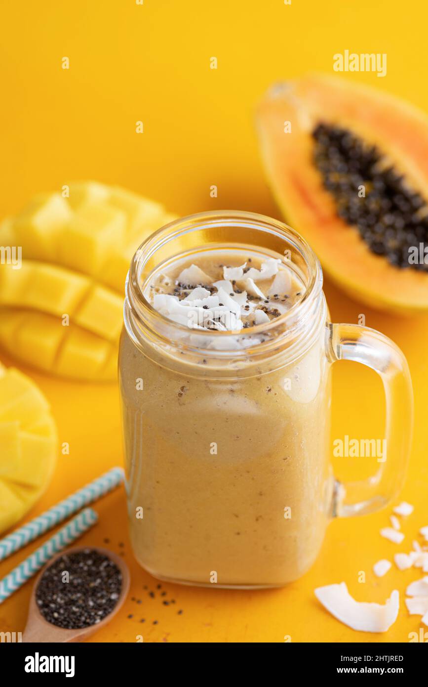 Delicious mango coconut smoothie, tropical fruit blended drink in glass on yellow background Stock Photo