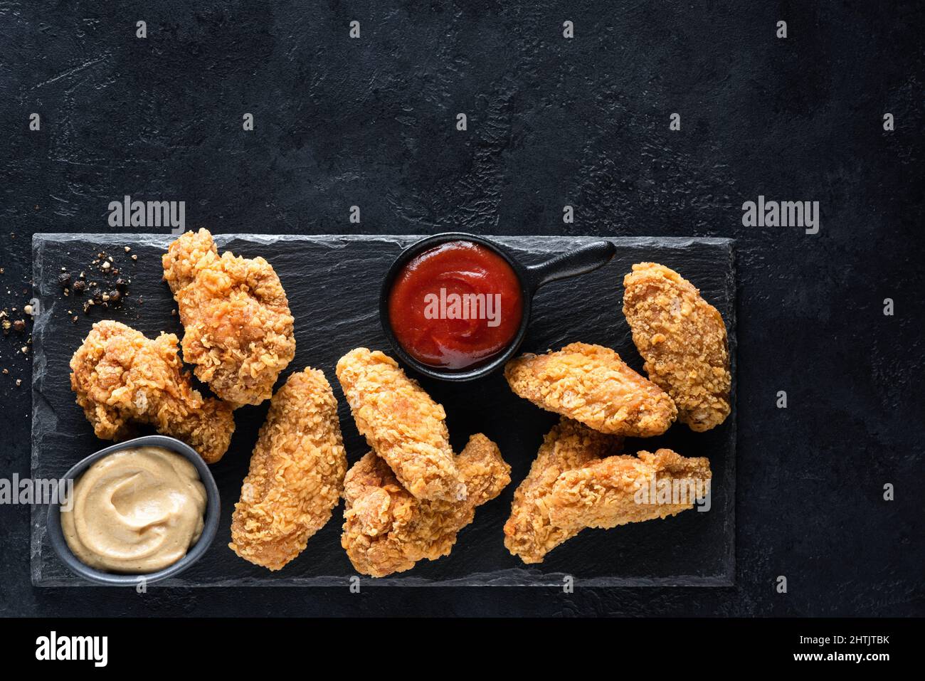 Fried chicken wings Kentucky style, crispy chicken served with sauces on black slate background. Top view copy space Stock Photo