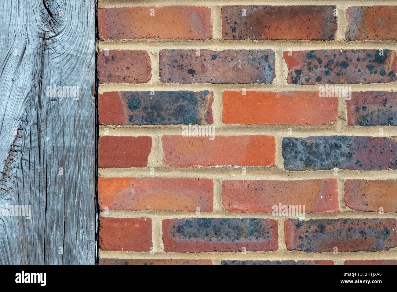 Close up section of mixed red brick wall, stretcher bond format with vertical wooden beam running through Stock Photo