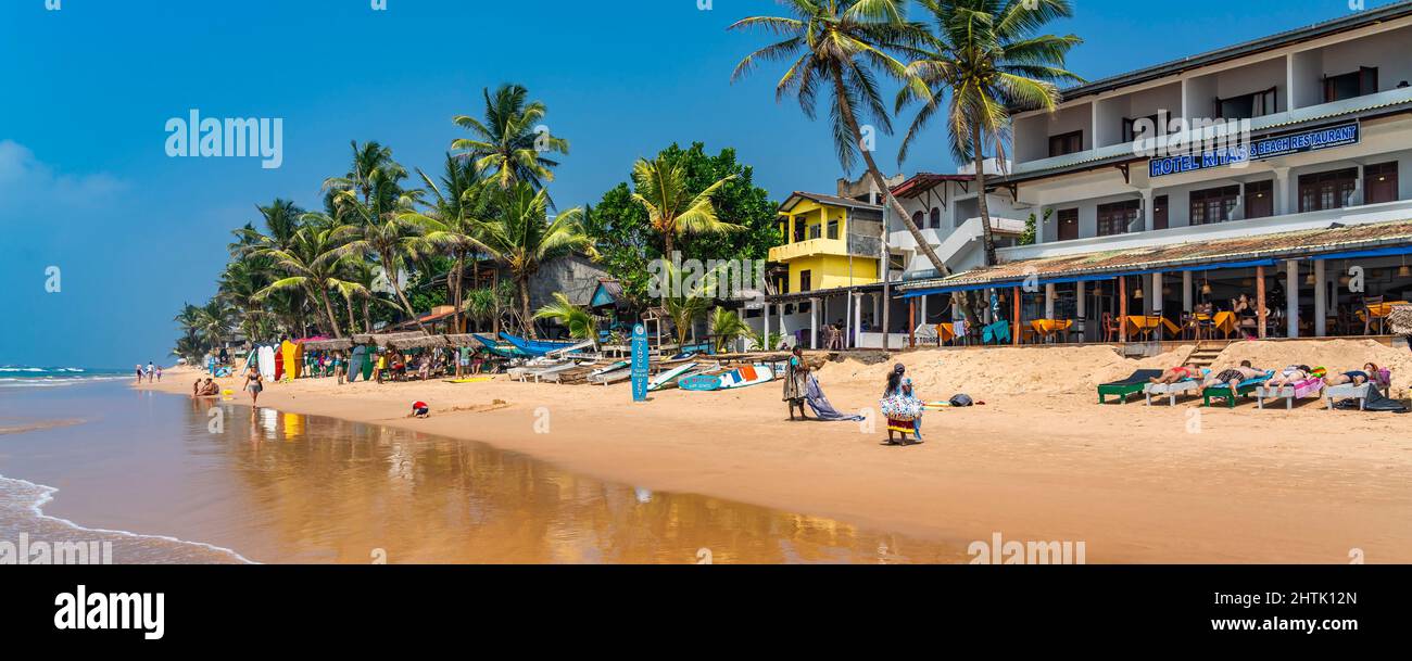 HIKKADUWA, SRI LANKA - JANUARY 22, 2022: Narigama beach at Hikkaduwa with people on sunbeds and small restaurants in background, panorama Stock Photo