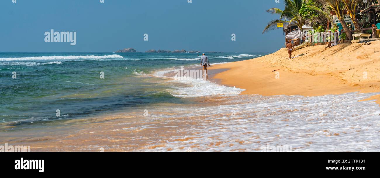 HIKKADUWA, SRI LANKA - JANUARY 22, 2022: Narigama beach at Hikkaduwa with a man walking along the shore, panorama Stock Photo