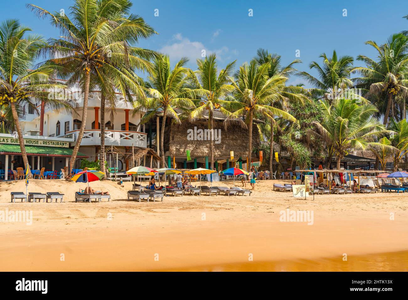 HIKKADUWA, SRI LANKA - JANUARY 22, 2022: Narigama beach at Hikkaduwa with people on sunbeds and small restaurants in background Stock Photo