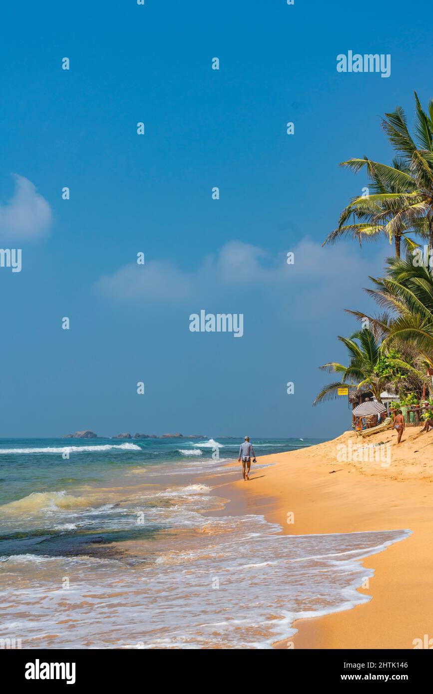 HIKKADUWA, SRI LANKA - JANUARY 22, 2022: Narigama beach at Hikkaduwa with a man walking along the shore, vertical Stock Photo