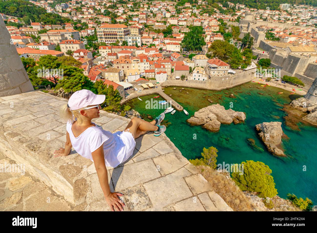 Woman resting on top walls of Fort Lovrijenac fort of Dubrovnik city in Croatia. Panorama of Dubrovnik walled city with Fort Bokar of Croatia in Stock Photo