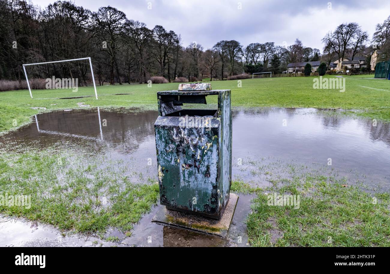 Reflection of the goalposts in the flood water says no football for a while, old litter bin damaged and neglected, Stock Photo