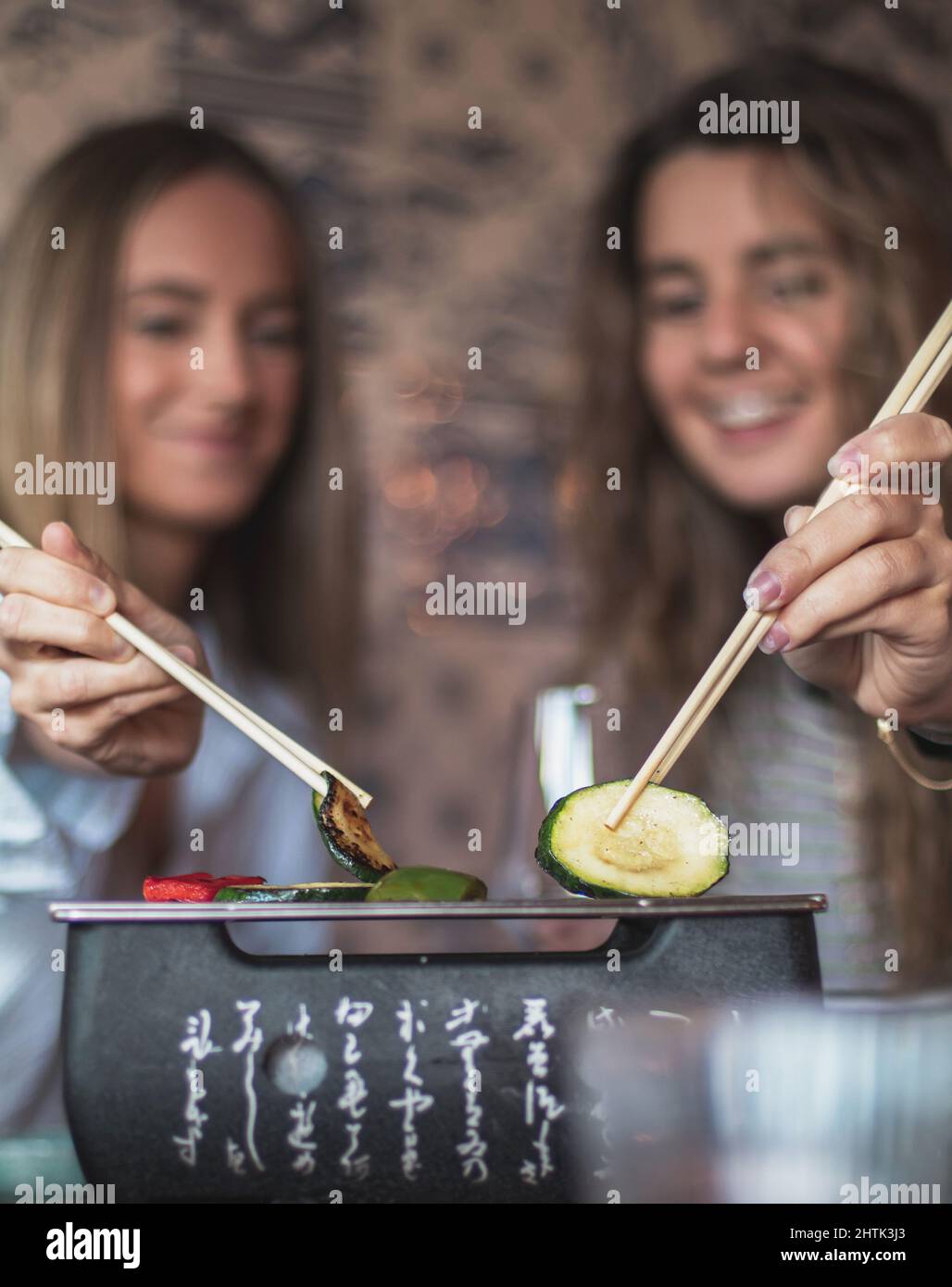 Selective focus of two happy customers female. enjoying and eating with chopsticks at japanese restaurant, hands close-up and blurry background. Stock Photo