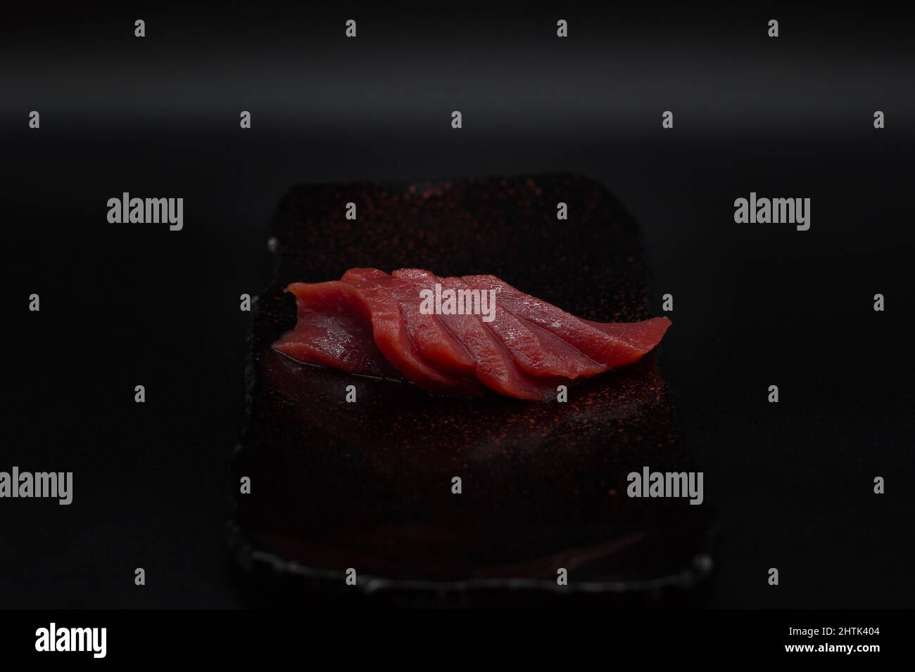 Traditional Japanese Sashimi cut, Raw and fresh Japanese Red Tuna sliced and served  in black plate with black background in a minimalist way. Stock Photo