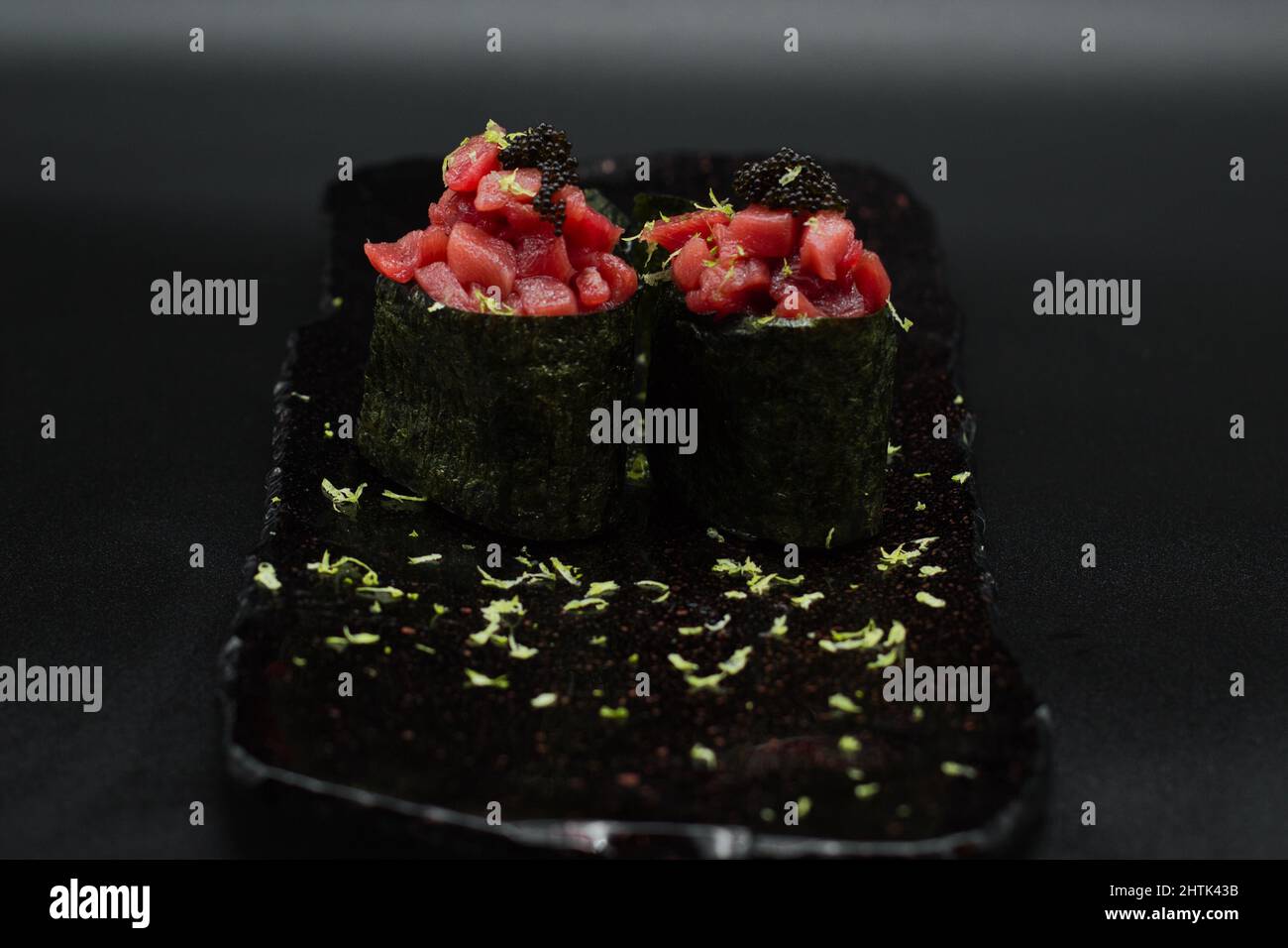 Traditional Japanese red tuna Gunkan, two pieces of raw tuna filet, fresh grated lime and black caviar served in black plate with black background. Stock Photo
