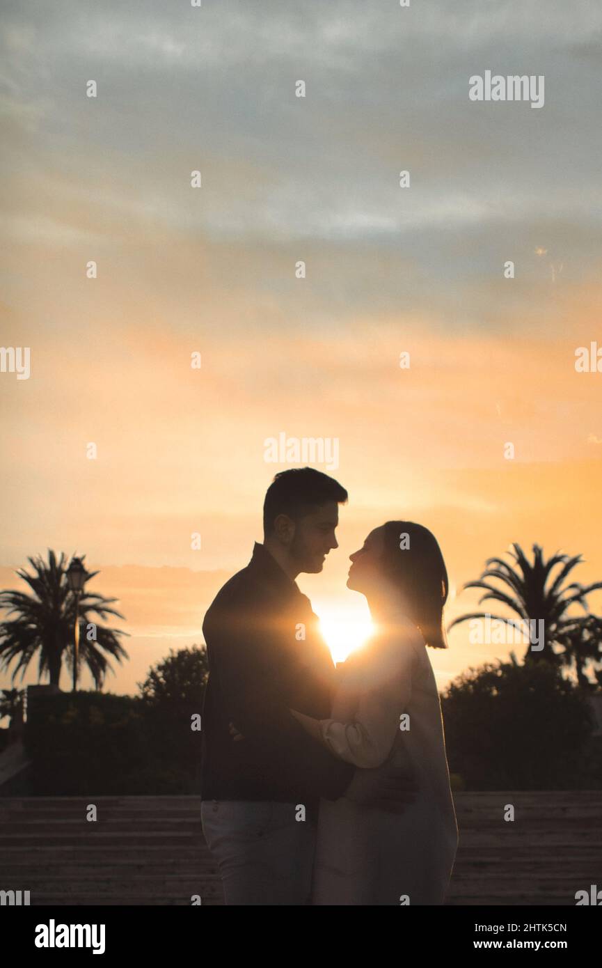 Silhouette of Romantic couple in love hugging and having eyes contact on a  sunset background with palms Stock Photo - Alamy