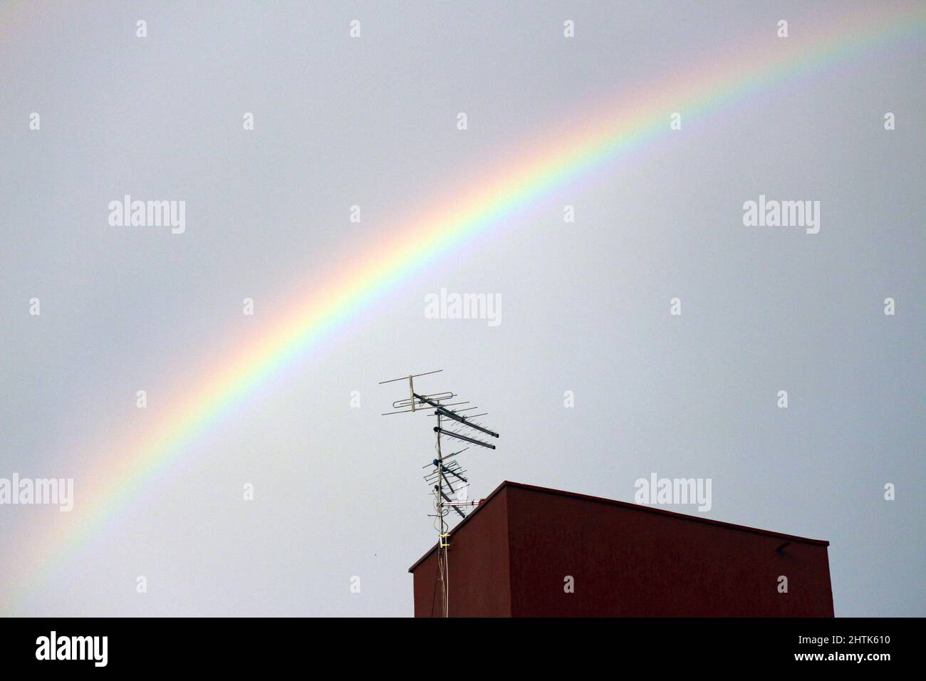 A rainbow crosses the sky over the details of urban life. Antennas, sources and construction. Stock Photo