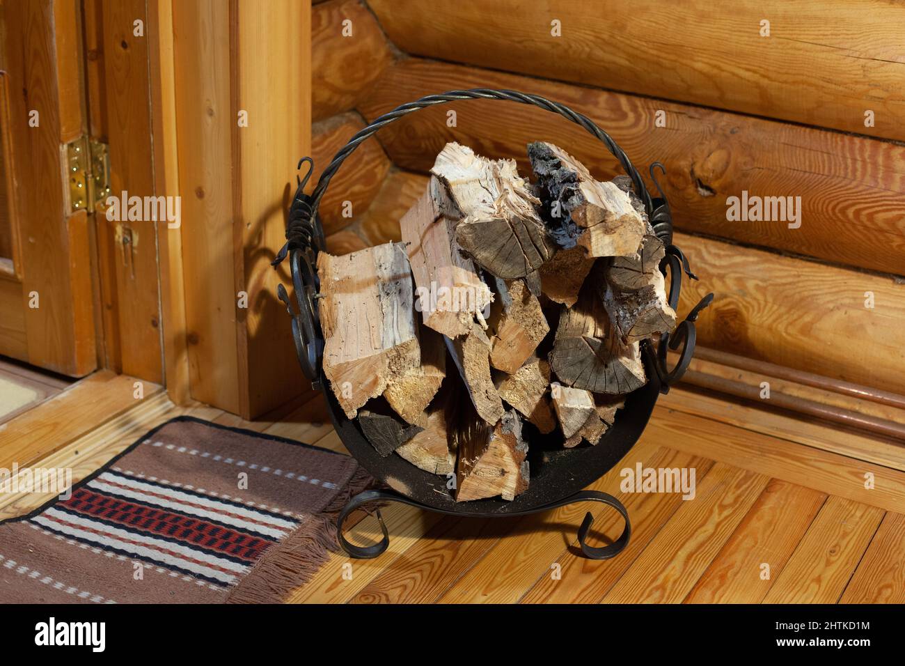 Black cast-iron forged woodpile with dozen of cut firewood for heating up sauna room. Having healthy rest time in bathhouse with friends during Stock Photo