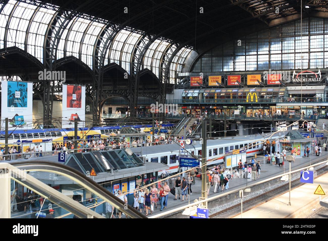 Interior of Wandelhalle, a large hall of Hamburg main railway or central train station in summer. Crowd of people waiting on platform for departure. Stock Photo