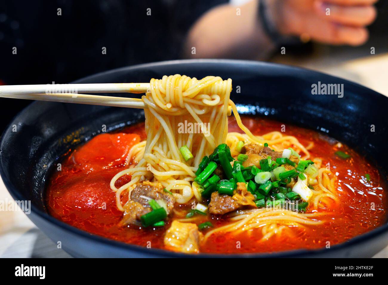 Chopstick pick up noddle from Chinese tomato beef noodle soup topped with green spring onions. Stock Photo