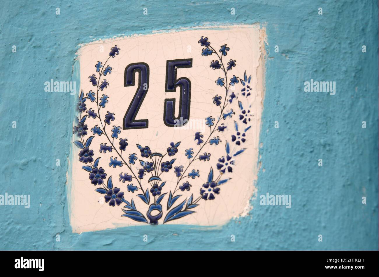 Street number 25 in a tile with ornaments in a blue paint wall Stock Photo