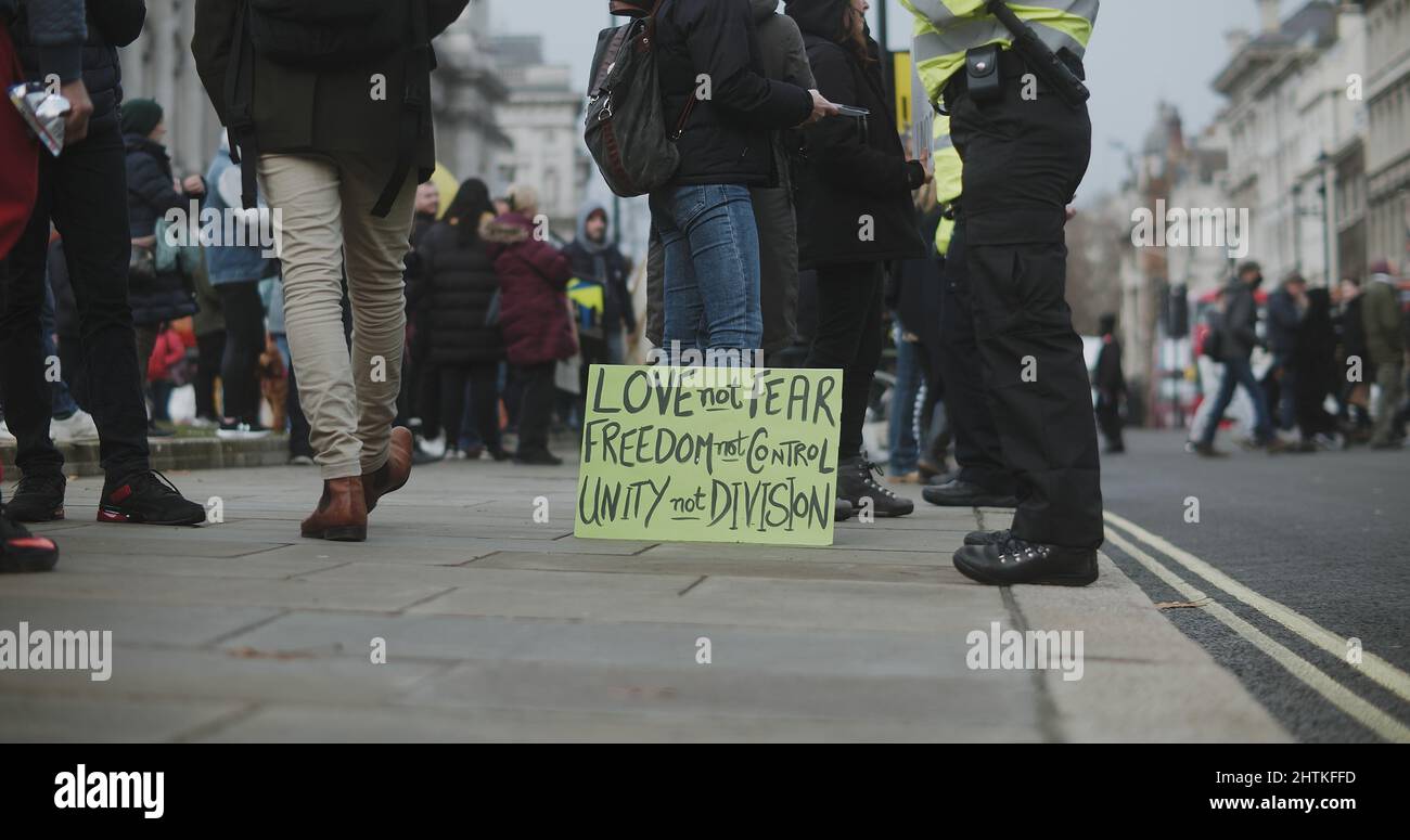 London, UK - 12 13 2021:  Police officer and protesters standing on the sidewalk with a sign, ‘Love not Fear, Freedom not Control, Unity not Division'. Stock Photo