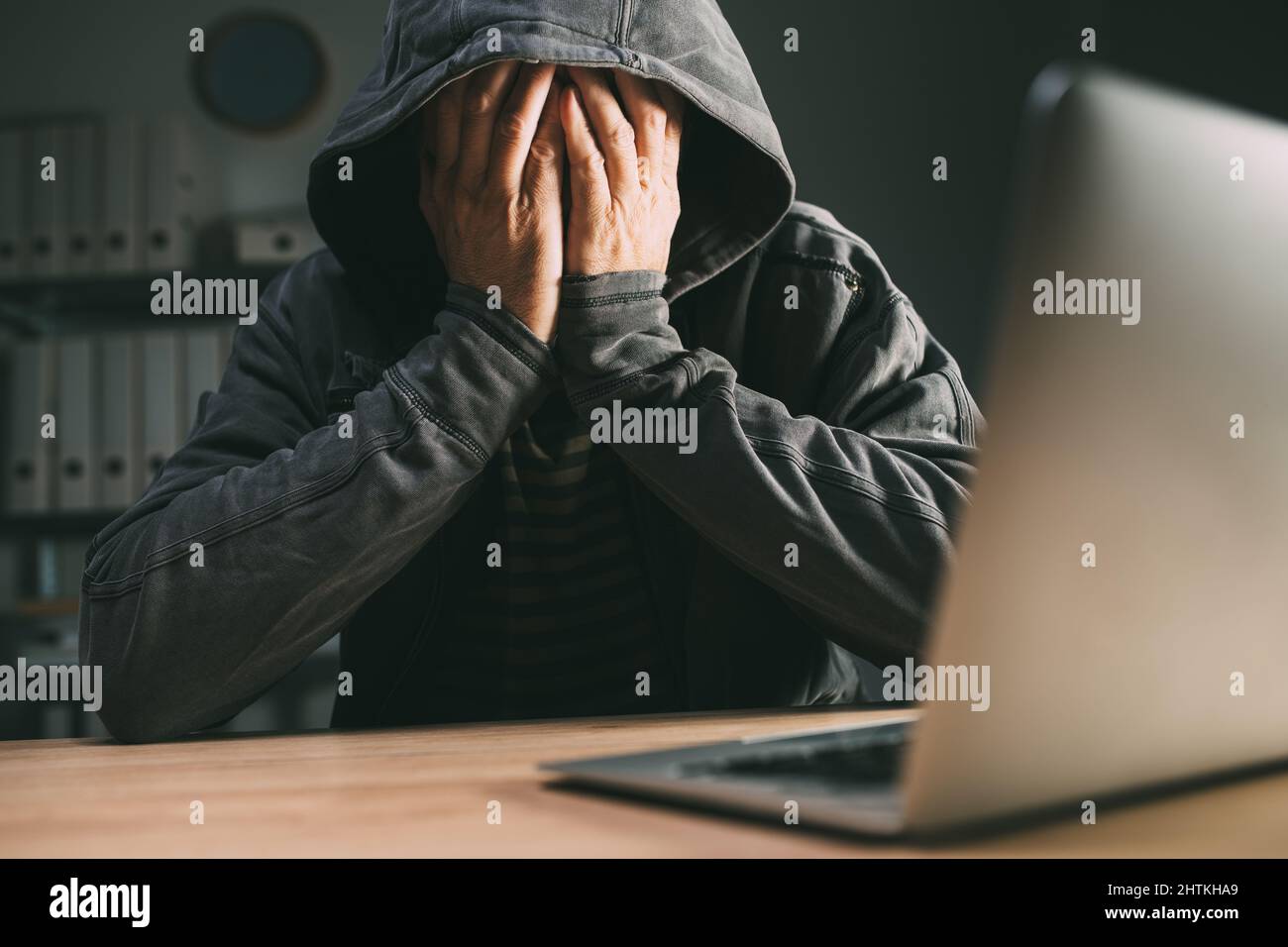Regretful computer hacker covering face with hands in front of laptop, selective focus Stock Photo
