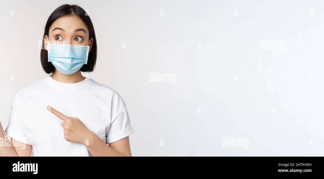Young korean woman in medical face mask pointing fingers left and