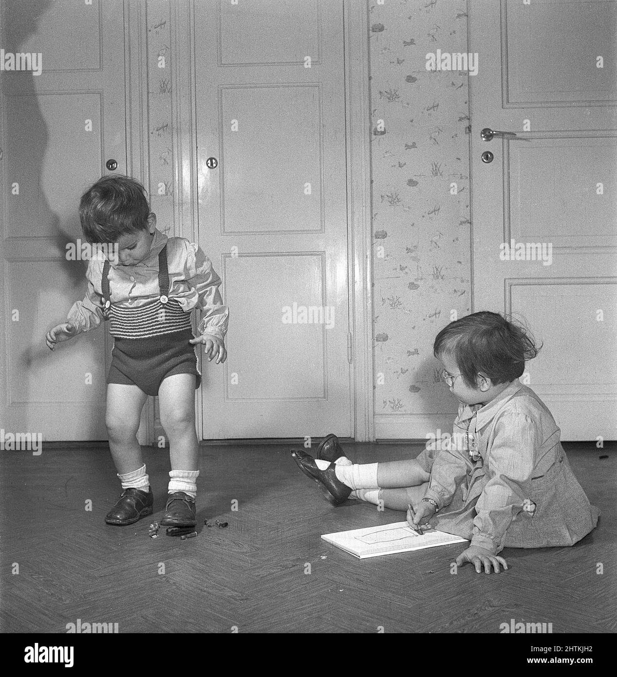 In the 1950s. Two children with crayons. The girl is creative and draws with it on a piece of paper while her brother thinks it's more fun to destroy them by crushing them with his foot. Sweden 1951. Kristoffersson BE41-11 Stock Photo