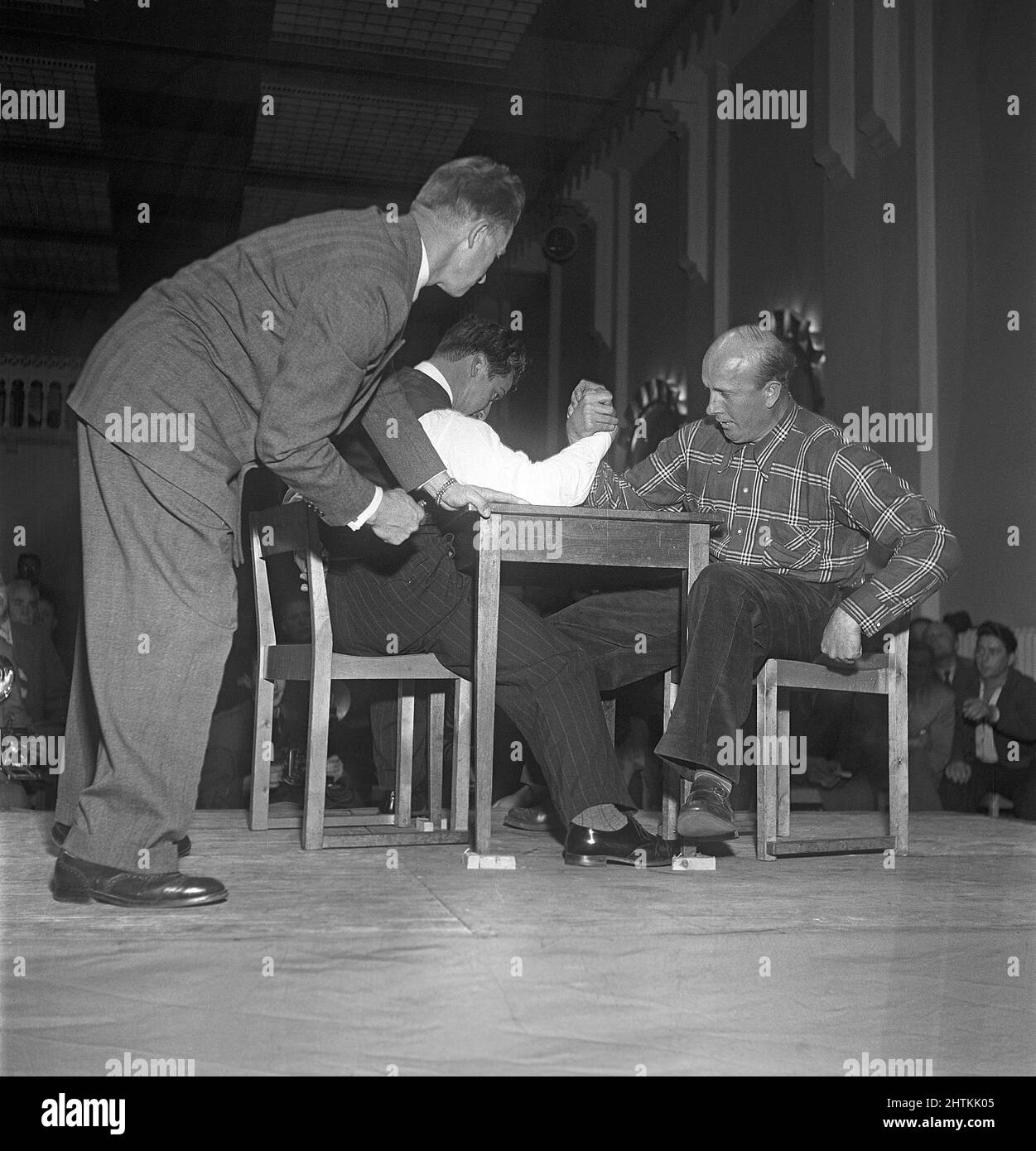 Who's the strongest? An armwrestling match is going on and it looks as the men are equally strong in this moment. The referee watches closely on.  Sweden 1951 Kristoffersson Ref BE34-9 Stock Photo