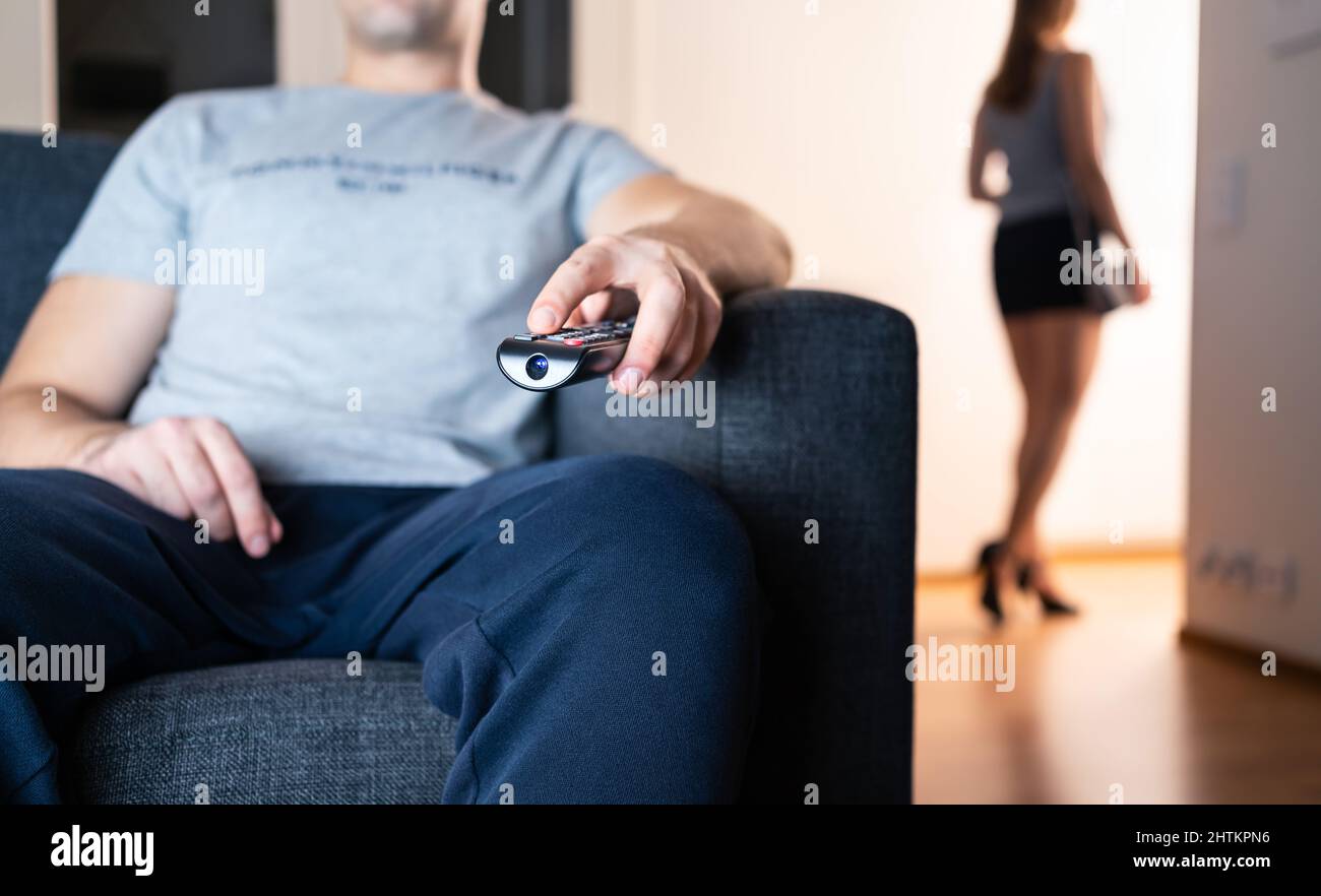 Distant couple ignore each other. Relationship fight, crisis or quarrel. Antisocial boring lazy man watching tv. Lonely sneaky woman leaving to party. Stock Photo