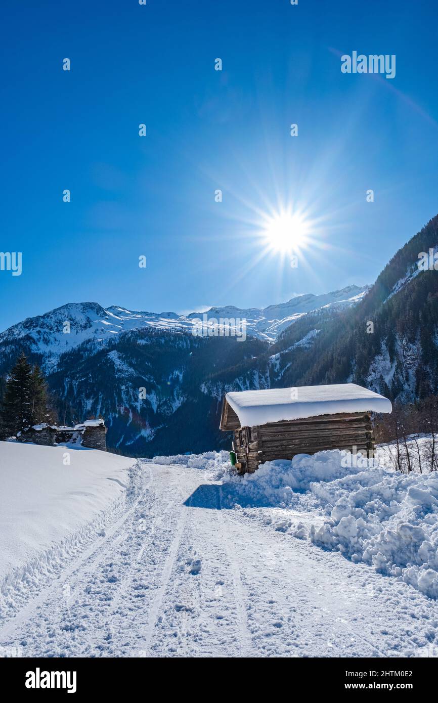 Wooden hut on a snow covered path under the bright sun in a snowy landscape with blue sky in ski resort Grossarlberg Salzburg Austria. Stock Photo