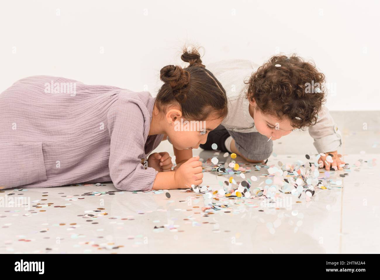 Happy girl and boy having fun together during birthday party with confetti. Cute children enjoying a holiday and throwing confetti. Stock Photo