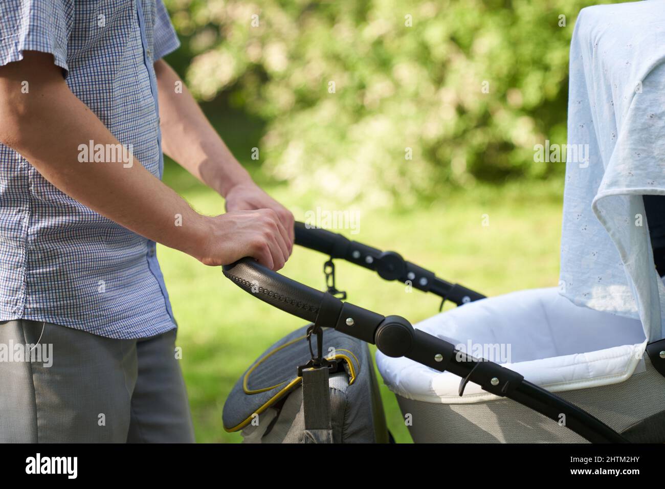 A young dad walking in the park with a baby in a stroller. Close-up of men's hands with a stroller. Father's Day concept. High quality photo Stock Photo