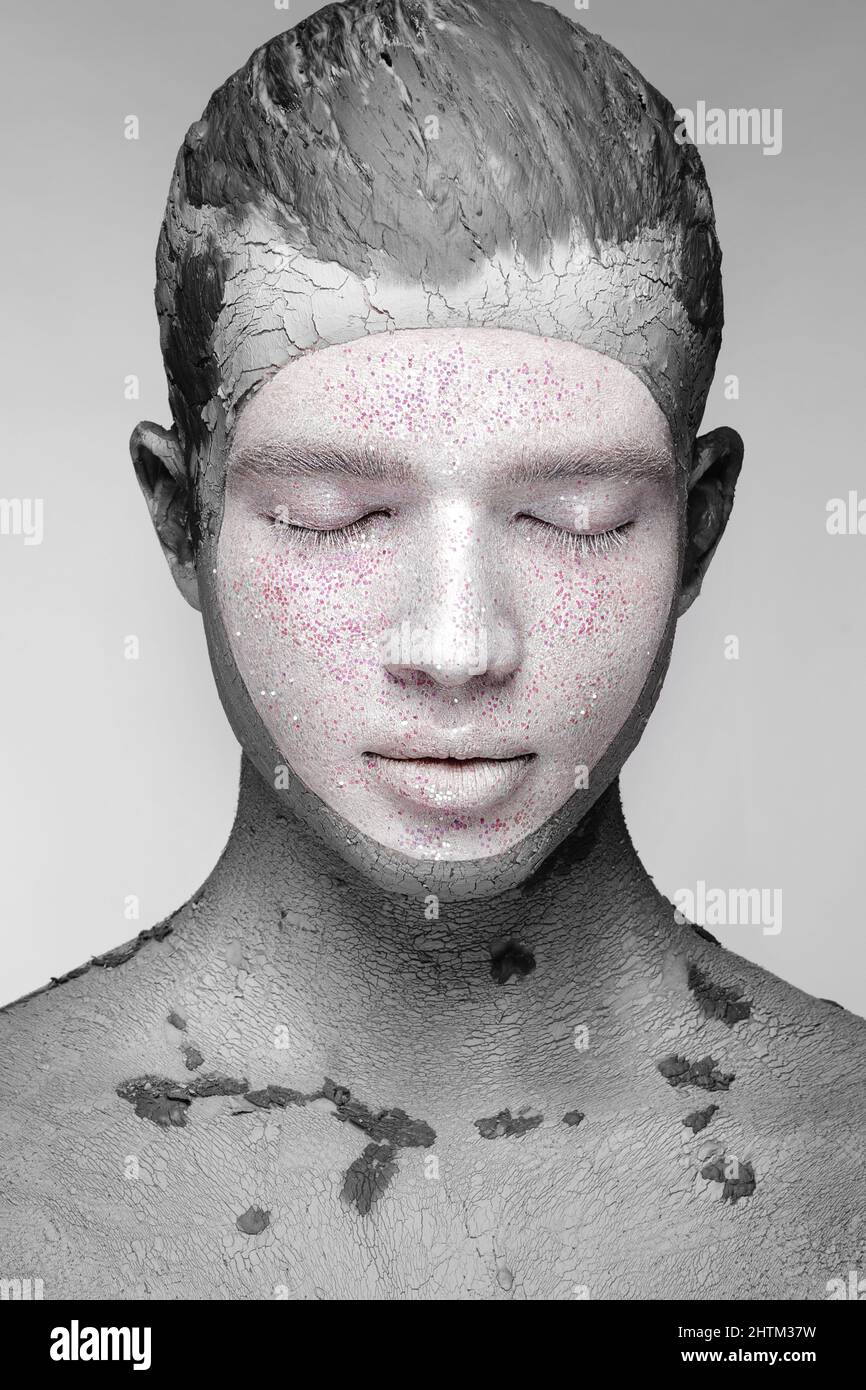 Young man with art creative make-up with mud on his face. Cosmetic mask. Stock Photo