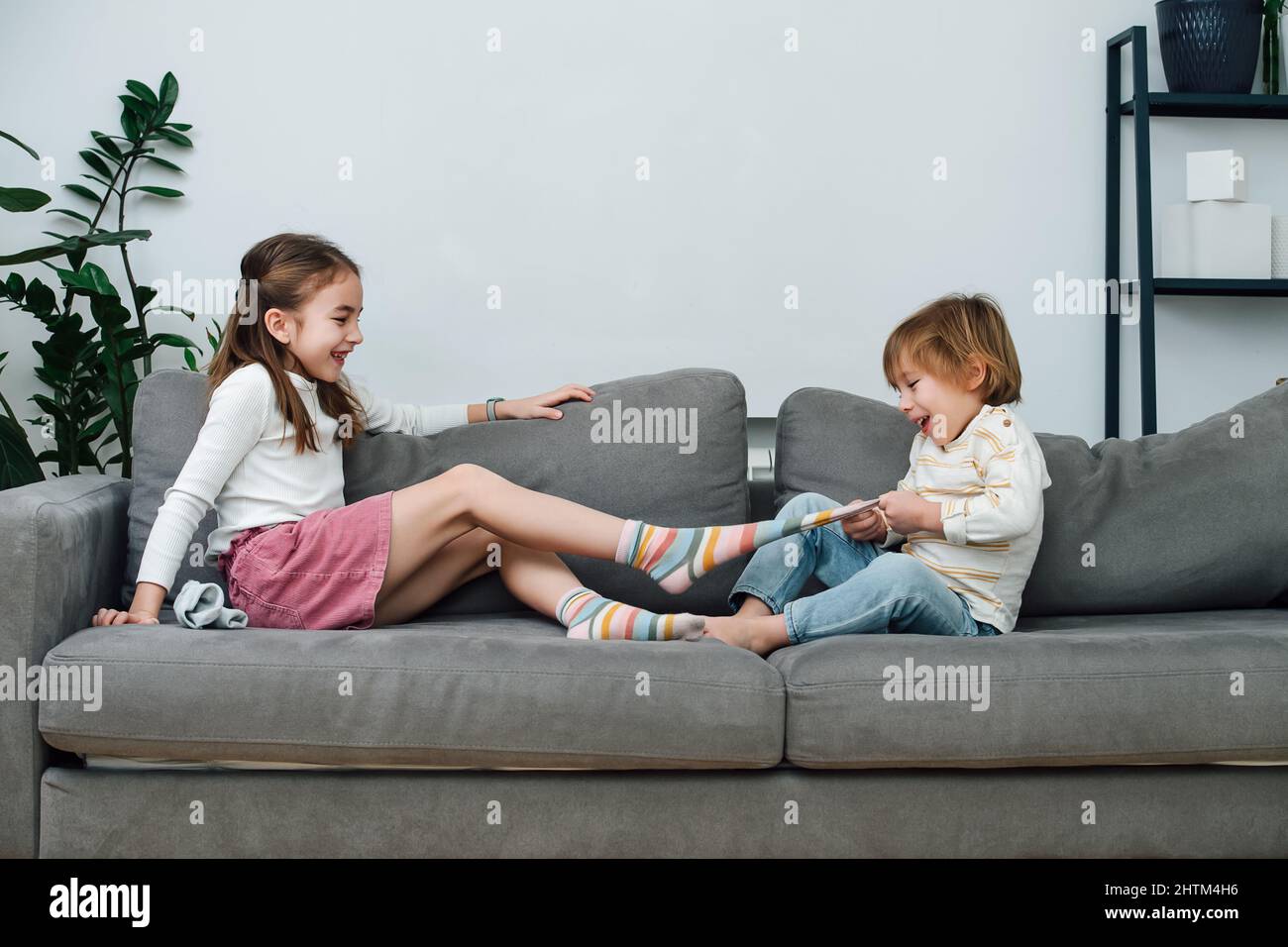 Boy pulling off sock of a girl, they are preparing for a tickling  competition. Sitting on a couch in a living room. Side view Stock Photo -  Alamy