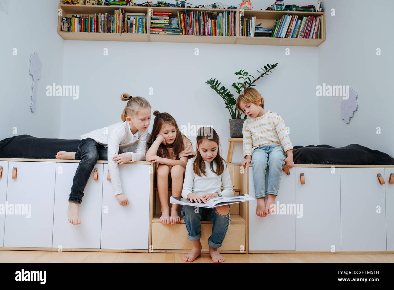 Group of children gathered in a room to read a picture book, all looking at it. From five to eight years of age. Stock Photo