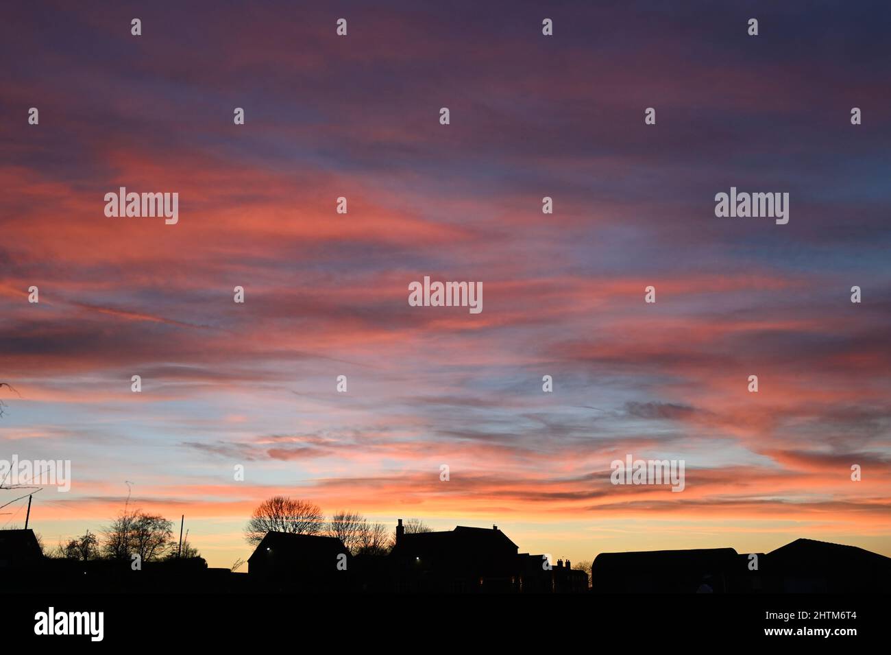 A beautiful sky sunset highlighting the red, oranges, purples and blue of the setting sun with the silhouette of a farm house and buildings Stock Photo