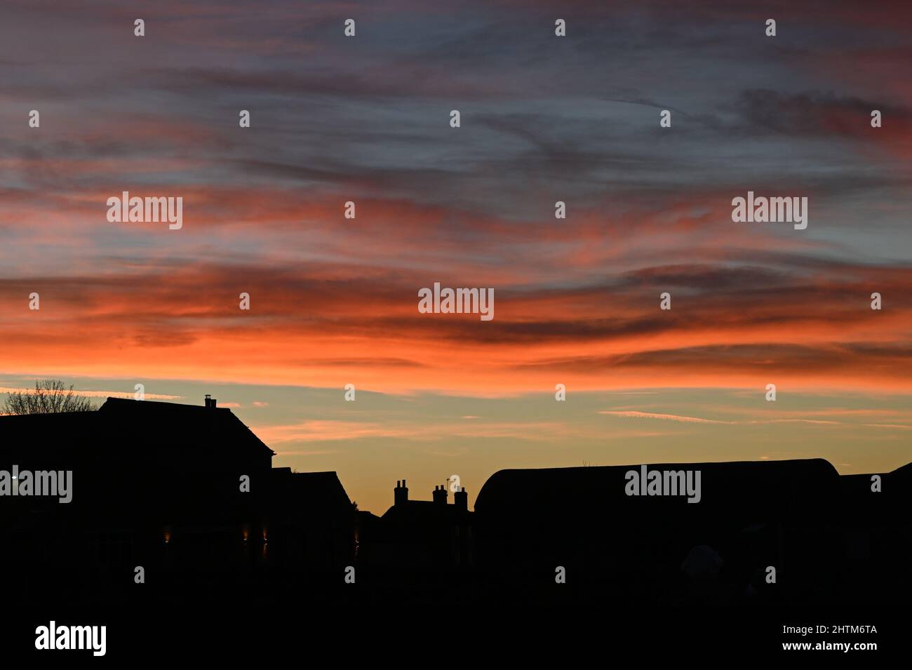 A beautiful sky sunset highlighting the red, oranges, purples and blue of the setting sun with the silhouette of a farm house and buildings Stock Photo