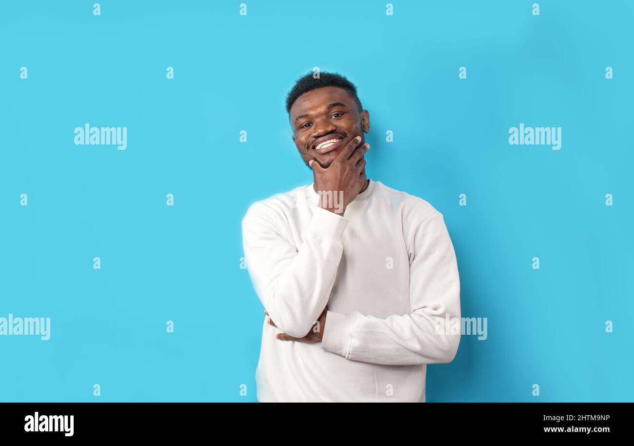 A young African-American man in a white T-shirt laughs on a blue isolated background Stock Photo