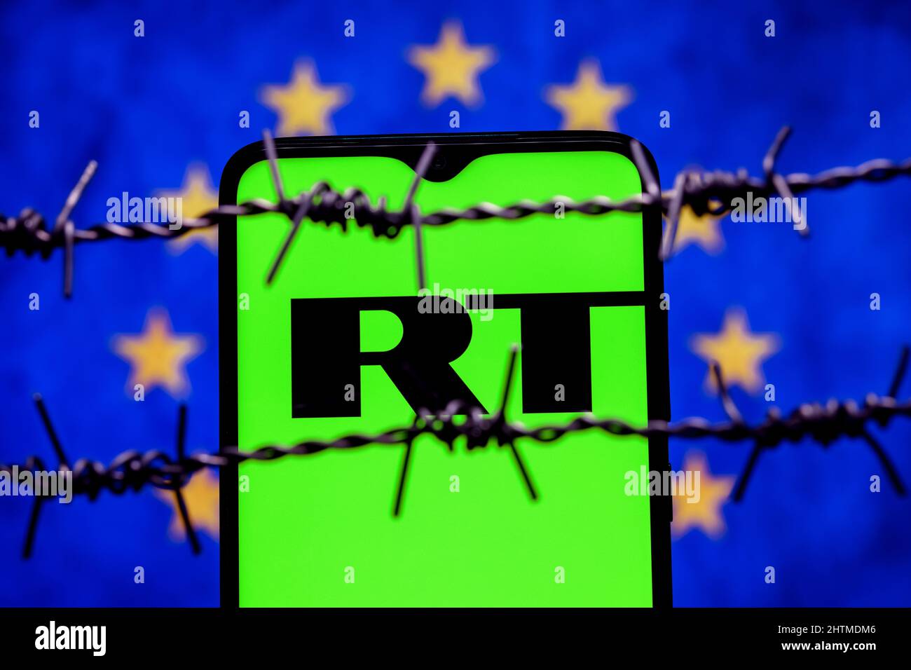 Smartphone with RT (Russia Today) logo on background of flag of European Union behind barbed wire Stock Photo