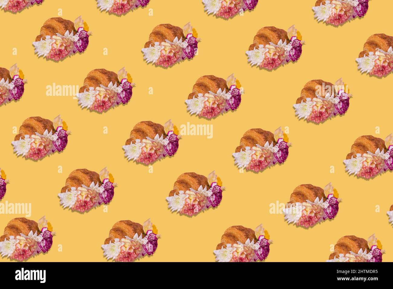 Creative pattern made of freshly baked croissant with flowers on pastel yellow background. Minimal spring or summer concept. Modern fun concept of sty Stock Photo