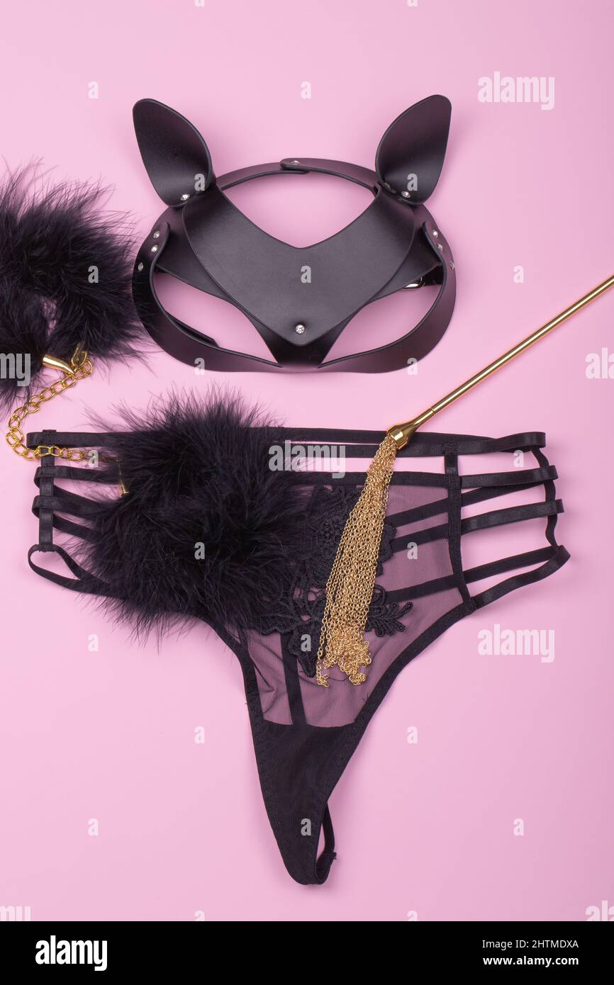 Lace sexy black womens underwear and set of erotic toys for BDSM. The game of sexual slavery with a whip, handcuffs and leather mask on a light pink b Stock Photo