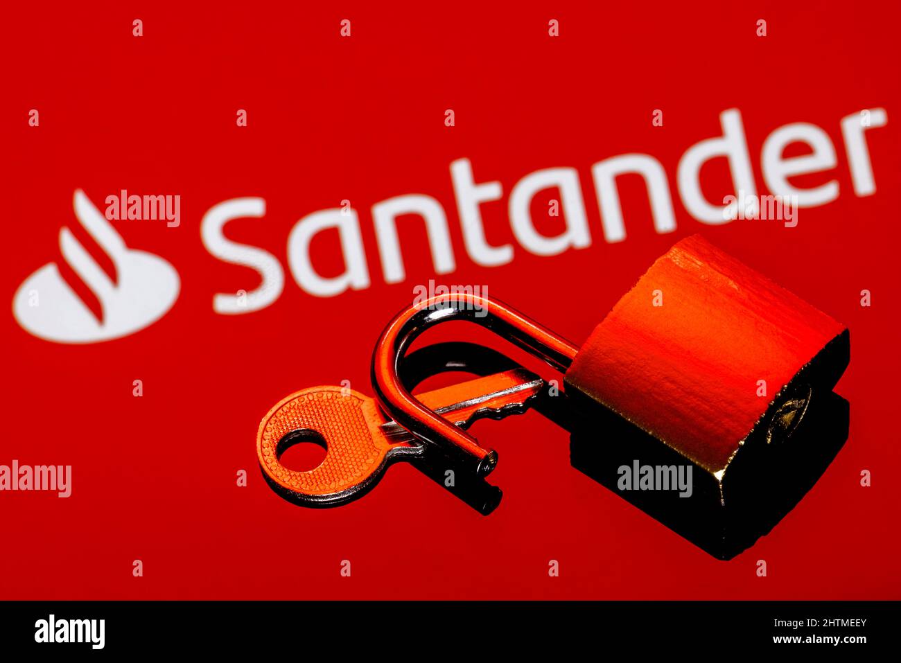 An open security lock and key on background of Santander bank logo in mirror reflection Stock Photo