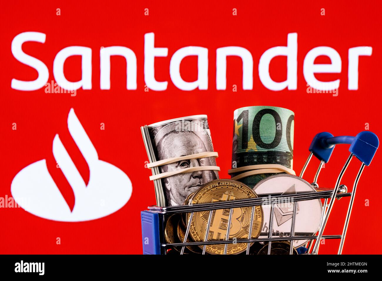 Crypto and traditional currencies in shopping cart on background of Santander bank logo Stock Photo