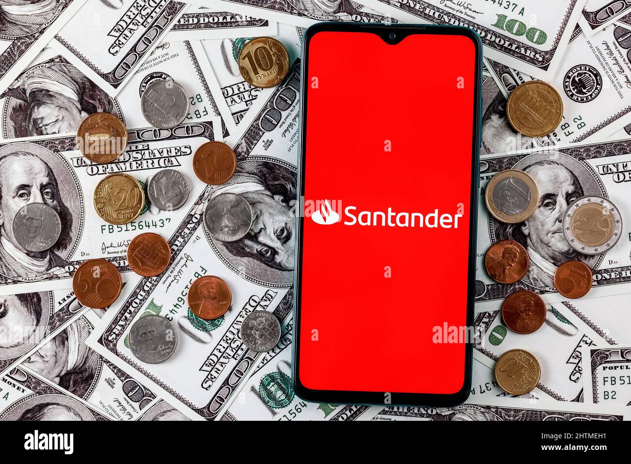 Smartphone with Santander bank logo surrounded by variety of metal coins on background of dollar bills Stock Photo