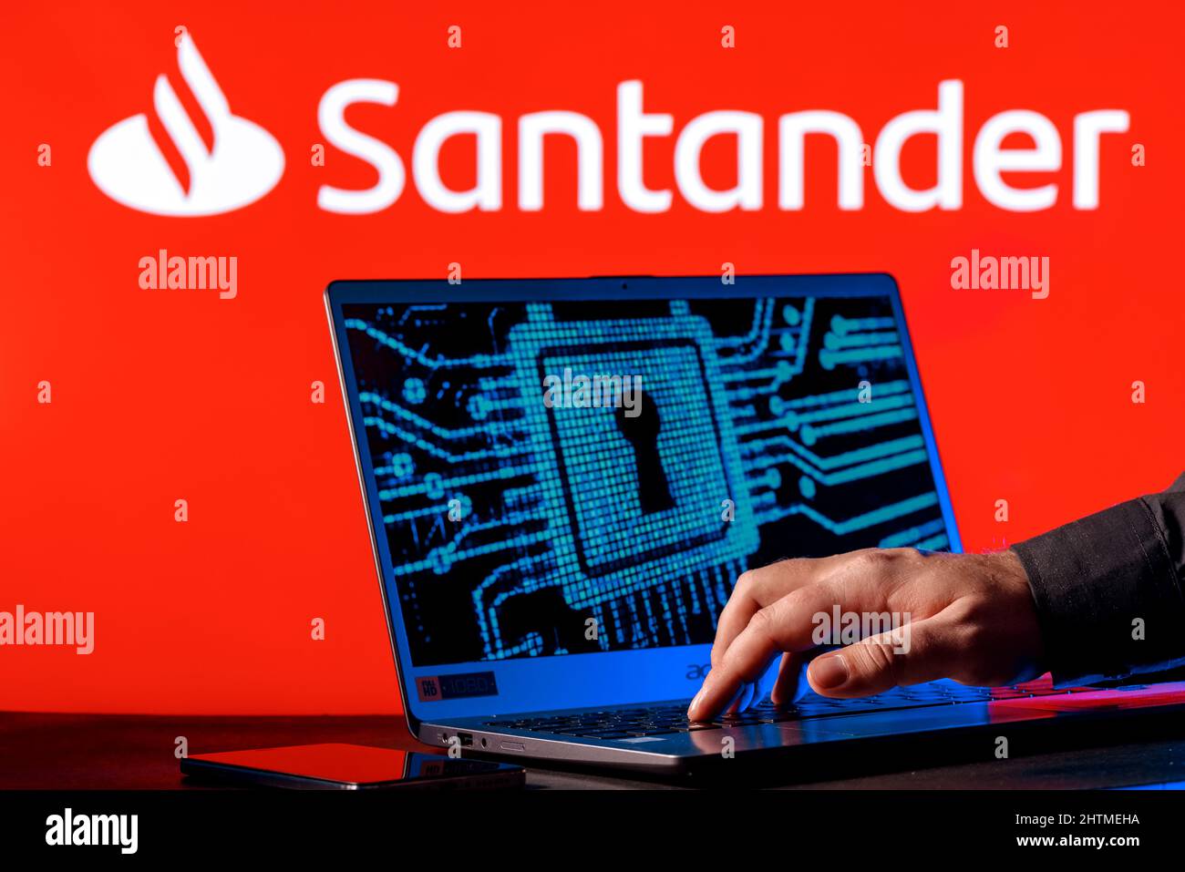 Laptop with lock symbol on screen on background of  Santander bank logo. Finger points to lock symbol. Concept of data hacking. Stock Photo