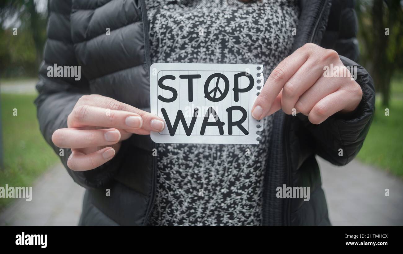 Approach to the hands of a Hispanic woman in the middle of a park holding in her hands a paper with the message STOP WAR in the foreground Stock Photo