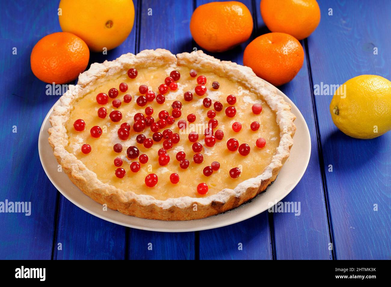 Tasty lemon pie decorated with fresh cranberries and whole orange, lemon and clementines on deep blue table  horizontal Stock Photo